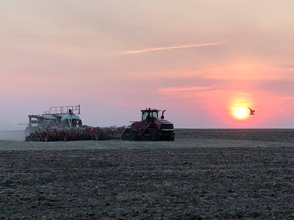 Dimly lit red tractor in foreground with fiery yellow sun setting in background