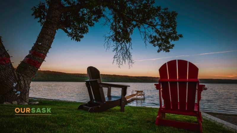 Sunrise at lake with a tree overhanging two red chairs in the foreground