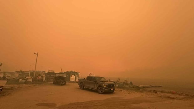 A photo of a truck and buildings under a smoky, dark orange sky.