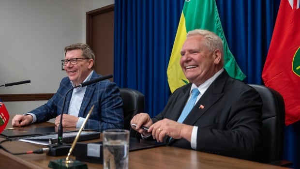 Two men smile as they sit side by side at a table.