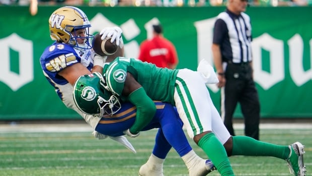 A football players in a green and white uniform tackles a player in a blue, white and gold uniform