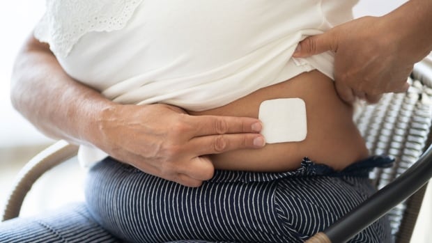 A woman applies an HRT patch to her abdomen.