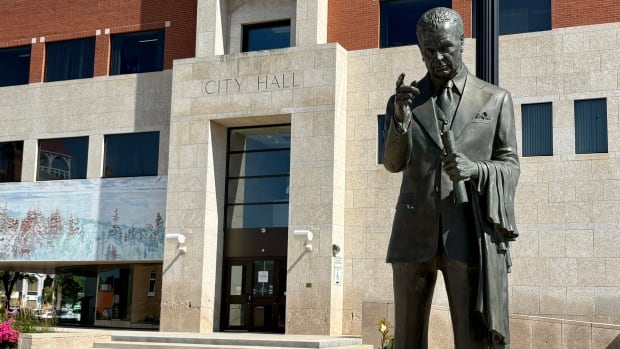 The main entrance of a building with the words City Hall chiseled into it and a statue in the foreground on a sunny summer day.