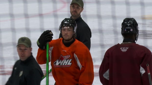 Two hockey players and two coaches stand idle on the ice.